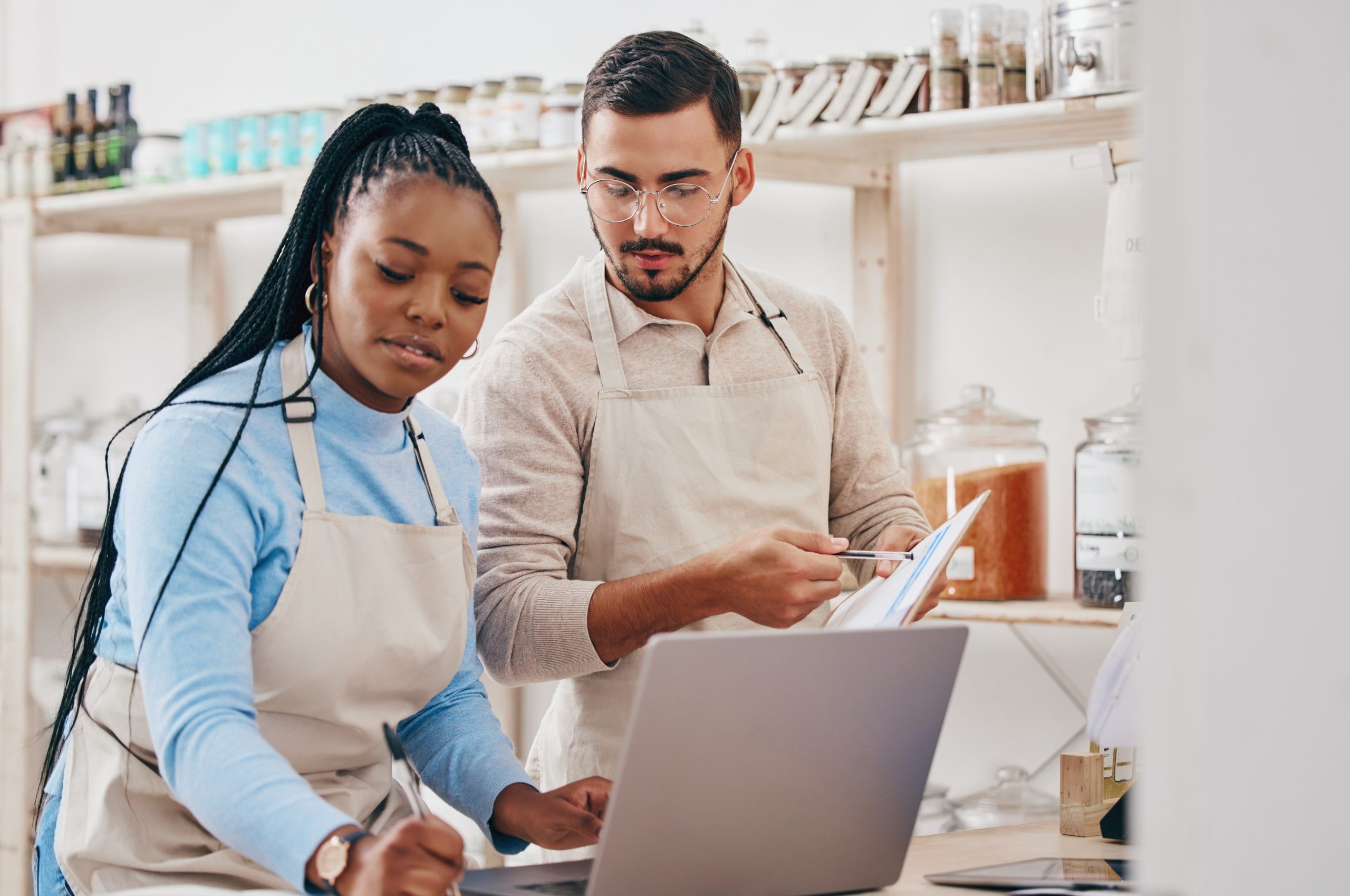 A male and a female retail store manager are entering data on a laptop