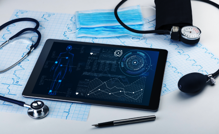 A tablet displaying a human anatomy diagram with analytics, placed on a table with a stethoscope, ECG graphs, a pen, and surgical masks