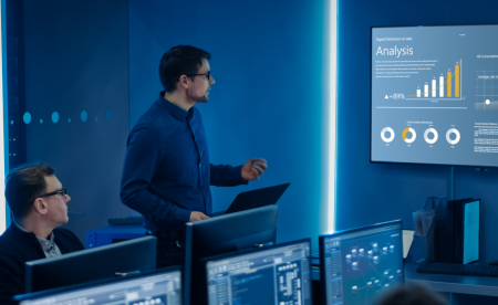 Two male IT professionals are analyzing data strategy on a large screen in a meeting room