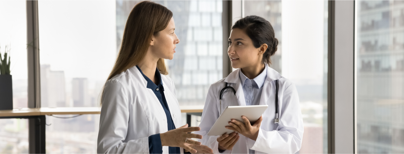 Two female healthcare professionals are discussing data using a tablet in a hospital setting