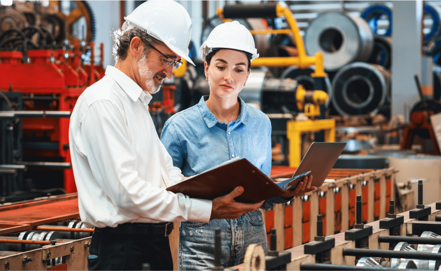 A male and a female manufacturing professional are discussing reports in a manufacturing industry setting