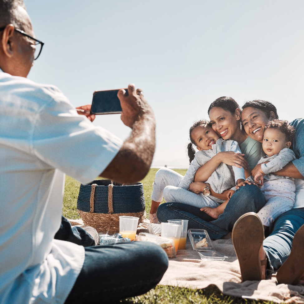 An old man is clicking the picture of two women holding their children in a garden picnic