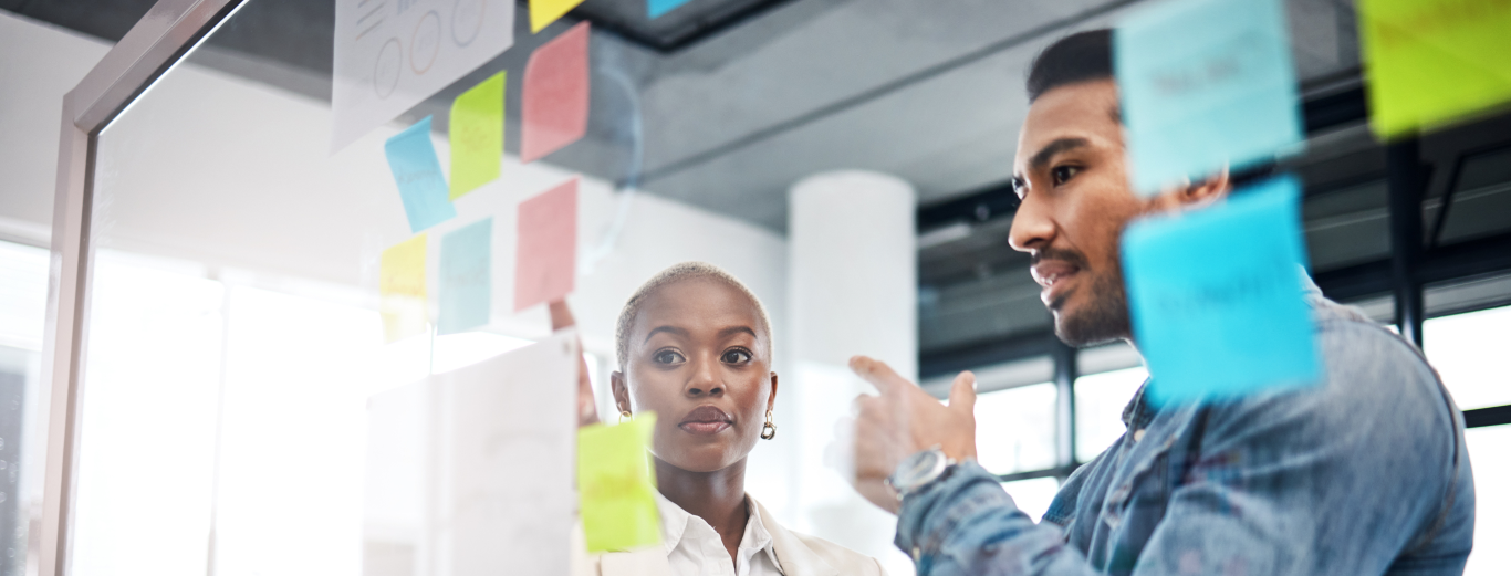 A male and a female IT professional are discussing data strategy on a vision board using sticky notes