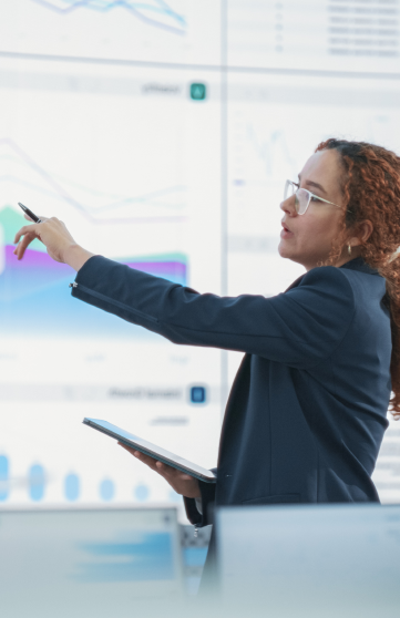 A female IT professional is analyzing data on a large screen in a conference room