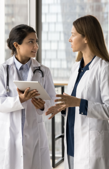 Two female healthcare professionals are discussing data using a tablet in a hospital setting