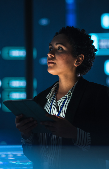 A female IT professional is analyzing data on large screens in a server room