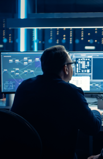 Two male engineers are analyzing code on multiple screens in a computer lab