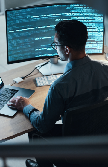 A male IT professional is working on computer screens to develop software code