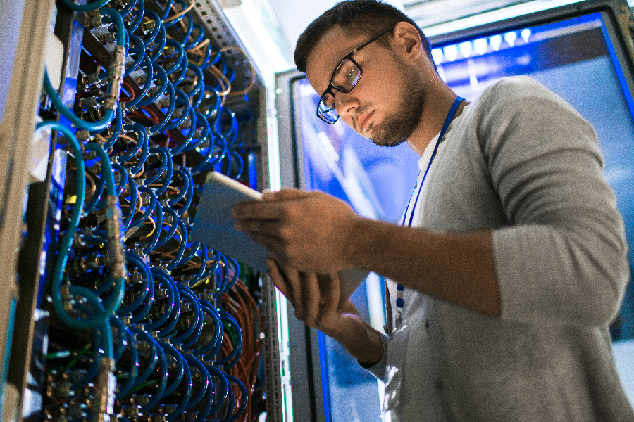 A male engineer is inspecting the servers using his tablet in a server room